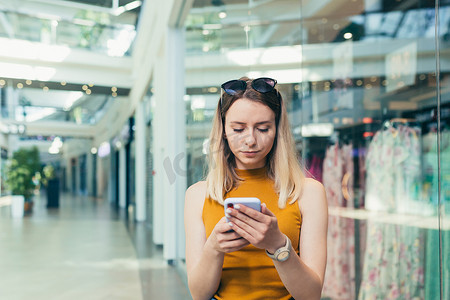 购物中心的年轻女性消费者使用智能手机浏览聊天和使用。