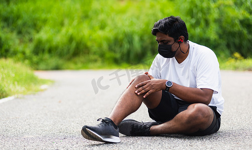 跑步的黑人男子戴着手表坐着，他在跑步时用手关节握住膝盖