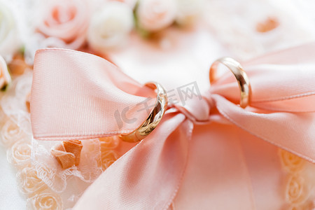 一对金色结婚戒指，在蕾丝面料上，配有玫瑰和蝴蝶结。