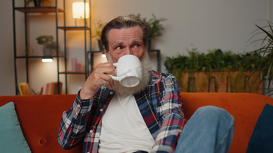 在家沙发上喝一杯咖啡或凉茶的迷人微笑老祖父
