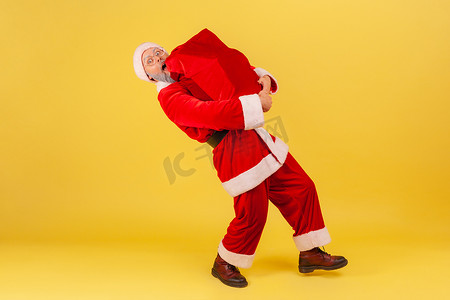 全长的灰胡子老人穿着圣诞老人服装，背着装着圣诞礼物的大袋子，祝贺新年。