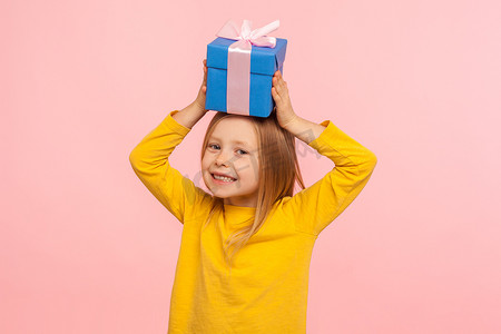 喜礼摄影照片_高兴的小女孩头上拿着礼盒，享受礼物，快乐地微笑的肖像