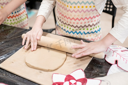儿童陶艺家用擀面杖在木桌上的一块特殊板上滚动棕色粘土来制作盘子。陶艺作坊。陶艺作坊。