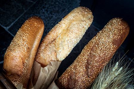 芝麻面包摄影照片_深色背景中 3 个带芝麻的新鲜小麦面包