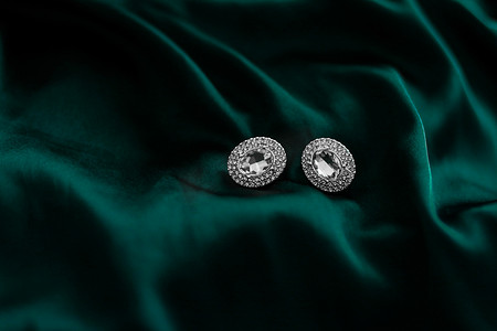 丝绸珠宝摄影照片_深翠绿色丝绸上的豪华钻石耳环，节日魅力珠宝礼物
