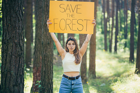 迎宾海报婚礼摄影照片_森林里年轻漂亮的女志愿者活动家，张贴着拯救森林的海报