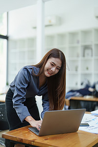 一位亚洲女员工第二天早上工作时面带微笑地站在电脑前的肖像