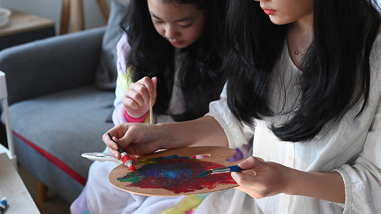 两个亚洲女孩在家里一起度过闲暇时光，用水彩画画。