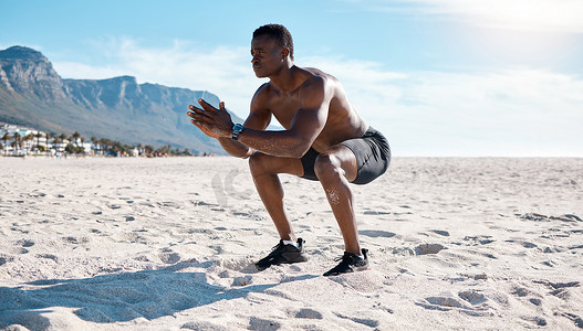 早上，年轻的黑人男子在海滩的沙子上进行深蹲练习。