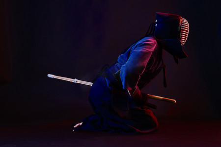 刀剑摄影照片_特写镜头，剑道战士穿着盔甲，传统和服，头盔练习武术与竹刀，黑色背景。