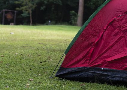 假期睡懒觉摄影照片_假期周末在田野绿草森林背景上的红色露营帐篷。