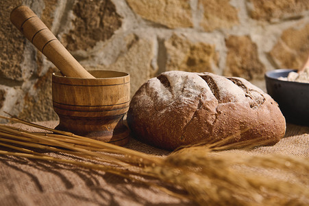 bre摄影照片_亚麻桌布上的传统全麦面包，旁边是木灰浆和前景模糊的小麦小穗