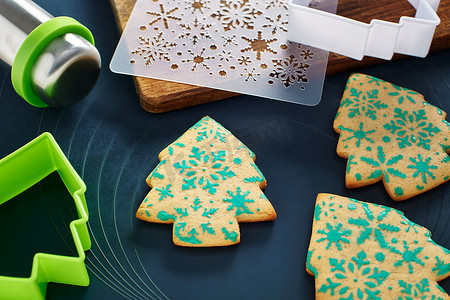 树形图案摄影照片_带有雪花图案的圣诞树形饼干、模板、饼干切割器、擀面杖、烤垫上的切板