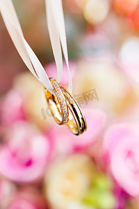 新娘花束上的金色结婚戒指，上面有粉色和黄色的玫瑰。