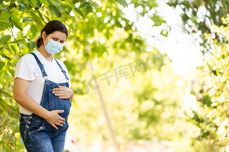 孕妇生病摄影照片_戴着防护口罩的年轻孕妇遮住了脸。