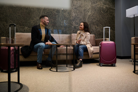 机场贵宾摄影照片_带着手提箱的已婚夫妇、商务旅行的合作伙伴在机场出发航站楼等待航班时在贵宾休息室会议室讨论计划和项目