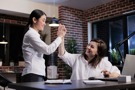 商业动力摄影照片_快乐积极进取的女商人在办公室工作区通过互相击掌来庆祝成功的商业交易。