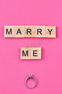 成婚摄影照片_订婚戒指的平躺顶视图和文字“嫁给我”在木制立方体上。