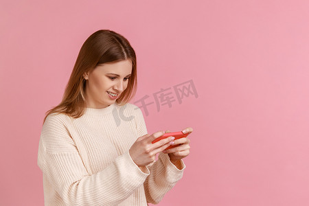 关卡游戏摄影照片_快乐积极的金发女人拿着智能手机，玩电子游戏，成功完成关卡。