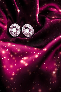 丝绸珠宝摄影照片_深红色丝绸上的奢华钻石耳环，雪光闪闪，节日冬季魔法珠宝礼物