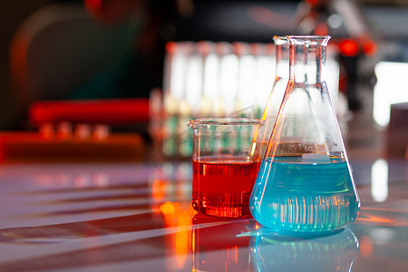 锥形烧瓶摄影照片_发光的实验室烧瓶，里面装满了五颜六色的化学溶液，桌子上有阴影。