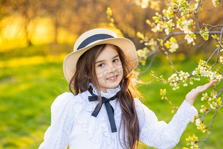 一个戴着帽子和白色镂空连衣裙的可爱女孩，​​手里拿着一棵开着白花的树枝