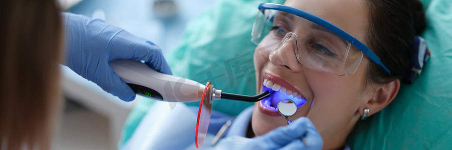 戴防护手套的年轻女牙医检查牙齿密封，在口腔手术过程中固定光聚合物灯