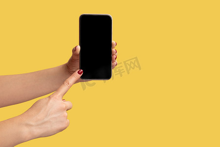 女性手持并显示智能手机并指向空显示屏的侧视图特写镜头。
