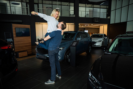 幸福的白人夫妇在汽车经销店购买新车时拥抱。