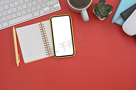 平躺手机、笔记本、咖啡杯和笔在红色背景上。