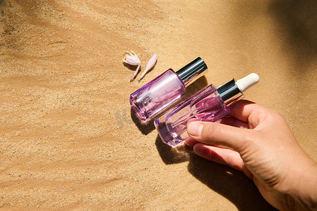 金沙背景浅紫色玻璃瓶中手放护肤美容产品包装的特写