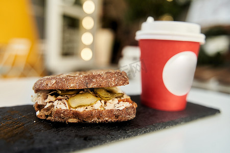 一家咖啡店的桌子上放着一个三明治，上面放着一杯红色塑料咖啡。