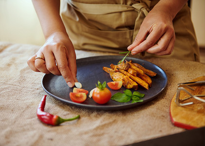 家庭主妇或厨师用樱桃番茄和烹饪香草装饰炸红薯菜肴的手特写