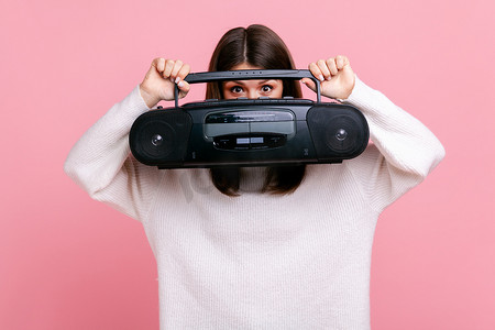 害羞的黑发女性的肖像拿着录音机，用电唱机遮住脸，向外窥视