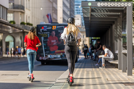 在城市环境中乘坐公共租赁电动滑板车的时尚时尚少女的后视图。