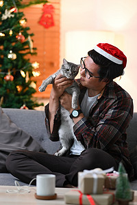 戴着圣诞老人帽子的男人在客厅里和他可爱的猫玩耍。