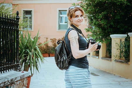 欧洲小镇摄影照片_美丽的女孩手里拿着胶片相机，走在一个古老的欧洲小镇的街道上。