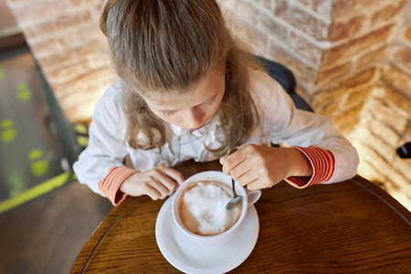 9、10 岁的女孩坐在咖啡厅的餐桌上，喝着一杯热巧克力
