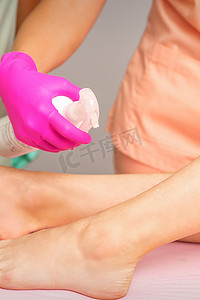 在脱毛手术之前，美容师在一名年轻女子的脚上喷洒消毒剂。