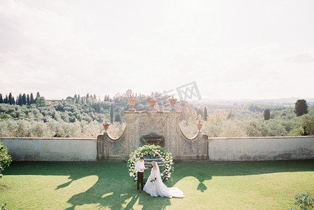 新娘和新郎站在石墙前的婚礼拱门附近
