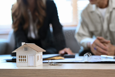 木桌上的房屋模型和财务顾问与老人在后台咨询合同抵押贷款。