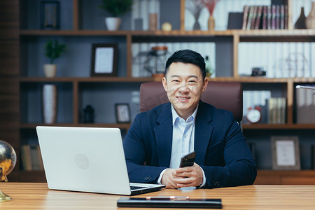 一位成功的亚洲人在经典办公室里用笔记本电脑微笑着工作的肖像