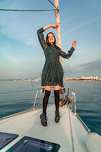 强风吹拂摄影照片_阳光明媚的夏日，女人站在游艇的鼻子上，微风吹拂着头发，背景是美丽的大海