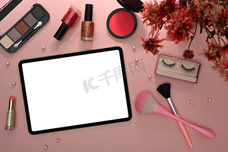 化妆小工具摄影照片_数字平板电脑、化妆刷、化妆品和粉红色背景的花朵。