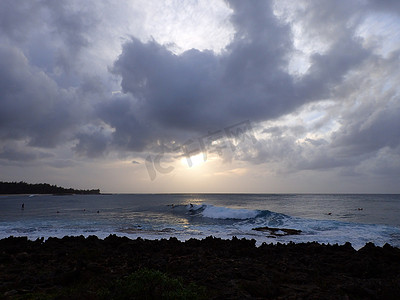 大海乘风破浪摄影照片_日落时分，冲浪者在海龟湾海岸的云层中乘风破浪