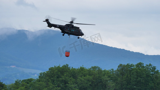 消防直升机飞越森林，提着装满水的水桶灭火