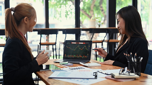 两位穿着正装的商务同事在笔记本电脑屏幕上分析股票图表，共同制定企业财务基金的交易策略