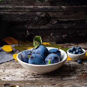 秋天的背景，在旧灰色木桌上的白色碗里放着成熟的紫蓝色李子，侧视
