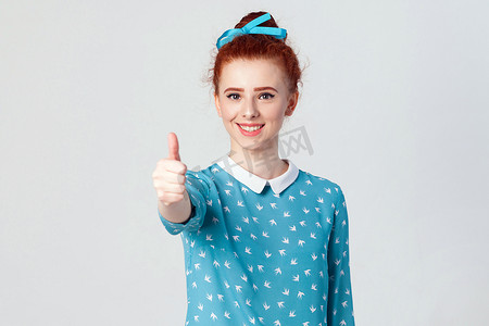 年轻快乐开朗的红发女孩竖起拇指和露齿微笑。