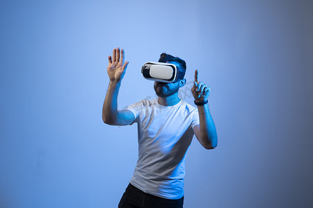 穿着白色 T 恤和 VR 眼镜的严肃的千禧一代男学生在虚拟现实世界中移动双手操纵手势。 